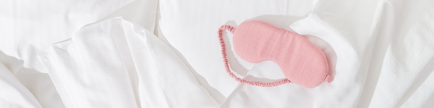 różowa opaska do spania leżąca na białej pościeli