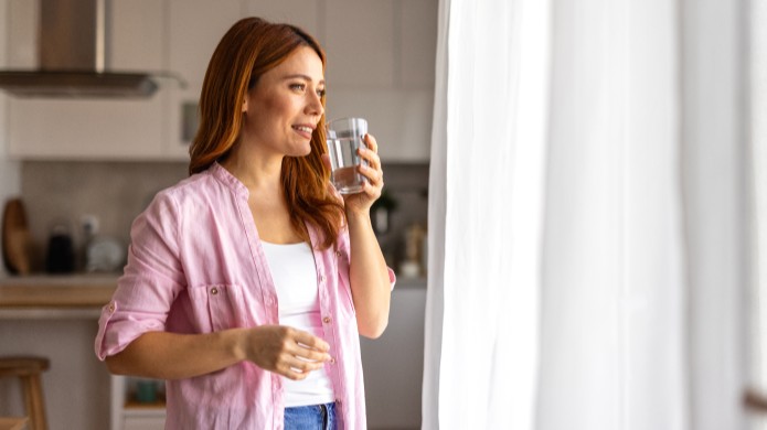 Dziewczyna w różowej koszuli pije wodę