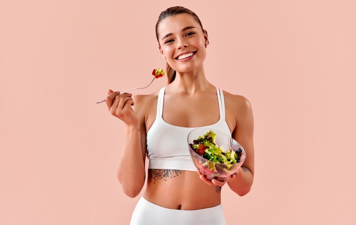 Dziewczyna w białym stroju sportowym je sałatkę