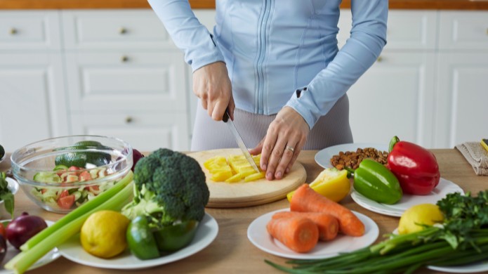 Kobieta w niebieskim stroju sportowym kroi warzywa i owoce