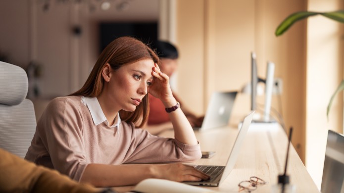 zamyślona kobieta siedzi przy biurku z laptopem, podpiera głowę ręką