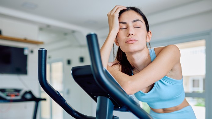 Zmęczona kobieta w niebieskim stroju sportowym zasnęła na bieżni