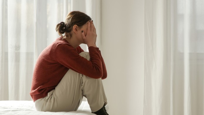 zestresowana kobieta, siedząca i trzymająca twarz w dłoniach